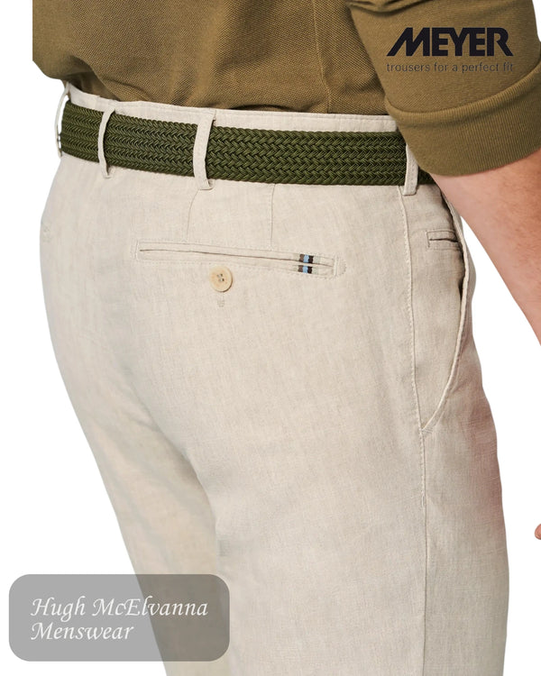 Beige pants with a green belt and a visible brand logo on a white background