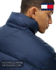 A close-up side profile of a man wearing a navy blue puffer jacket with a high collar, featuring the Tommy Jeans logo.