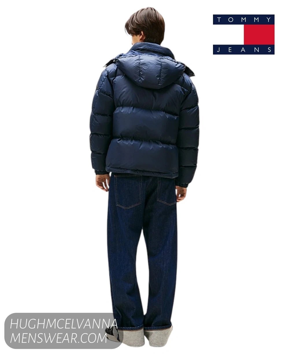 A man shown from the back wearing a navy blue puffer jacket and dark blue jeans, with the Tommy Jeans logo in the top right corner.
