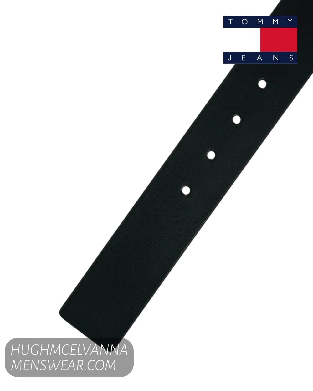 A close-up of a black leather belt strap with silver-toned metal eyelets, shown diagonally on a white background with a Tommy Jeans logo in the top right corner.