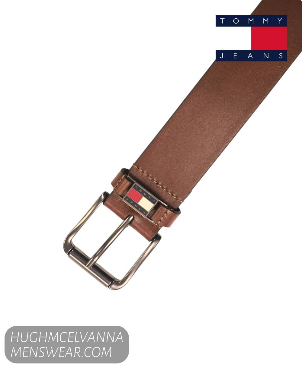 A brown leather belt with a silver-tone metal buckle, shown on a plain white background. The Tommy Jeans logo is visible in the top right corner, and a website watermark is in the bottom left.
