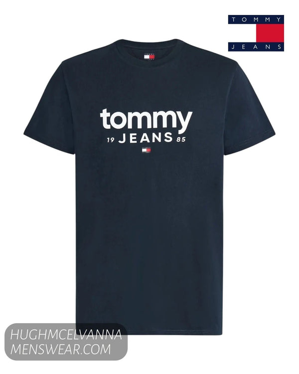 Flat lay product display of Tommy Jeans navy t-shirt featuring white 1985 logo print and flag emblem