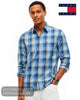 A man wearing a blue and white plaid long-sleeve button-down shirt by Tommy Jeans, paired with white trousers. 