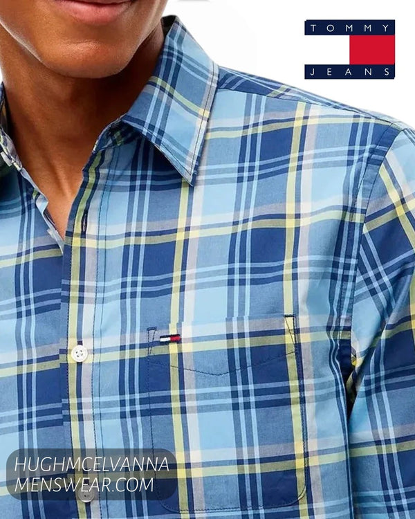 A close-up of a man wearing a Tommy Jeans plaid button-down shirt in shades of blue, navy, and yellow. 