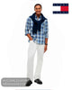 A man modeling a blue and white plaid button-down shirt with a navy blue knit sweater draped over his shoulders, paired with white trousers and black loafers.